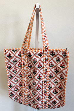 Red, peach floral tote bag with a geometric pattern hanging on a white wall.

