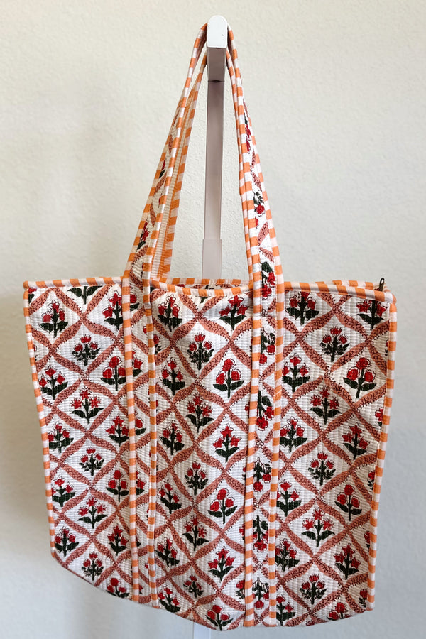 Red, peach floral tote bag with a geometric pattern hanging on a white wall.
